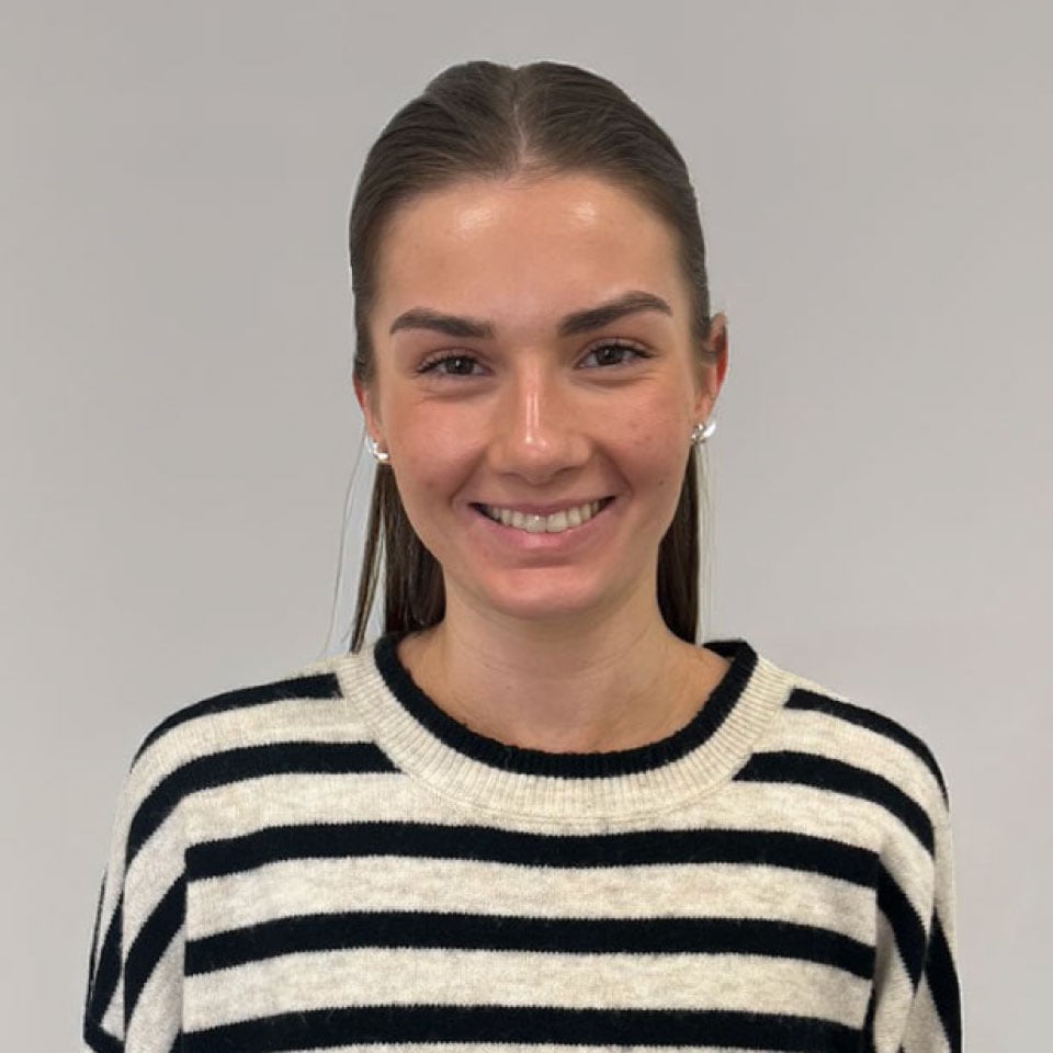 Smiling young woman with dark hair pulled back, wearing a black-and-white striped sweater.