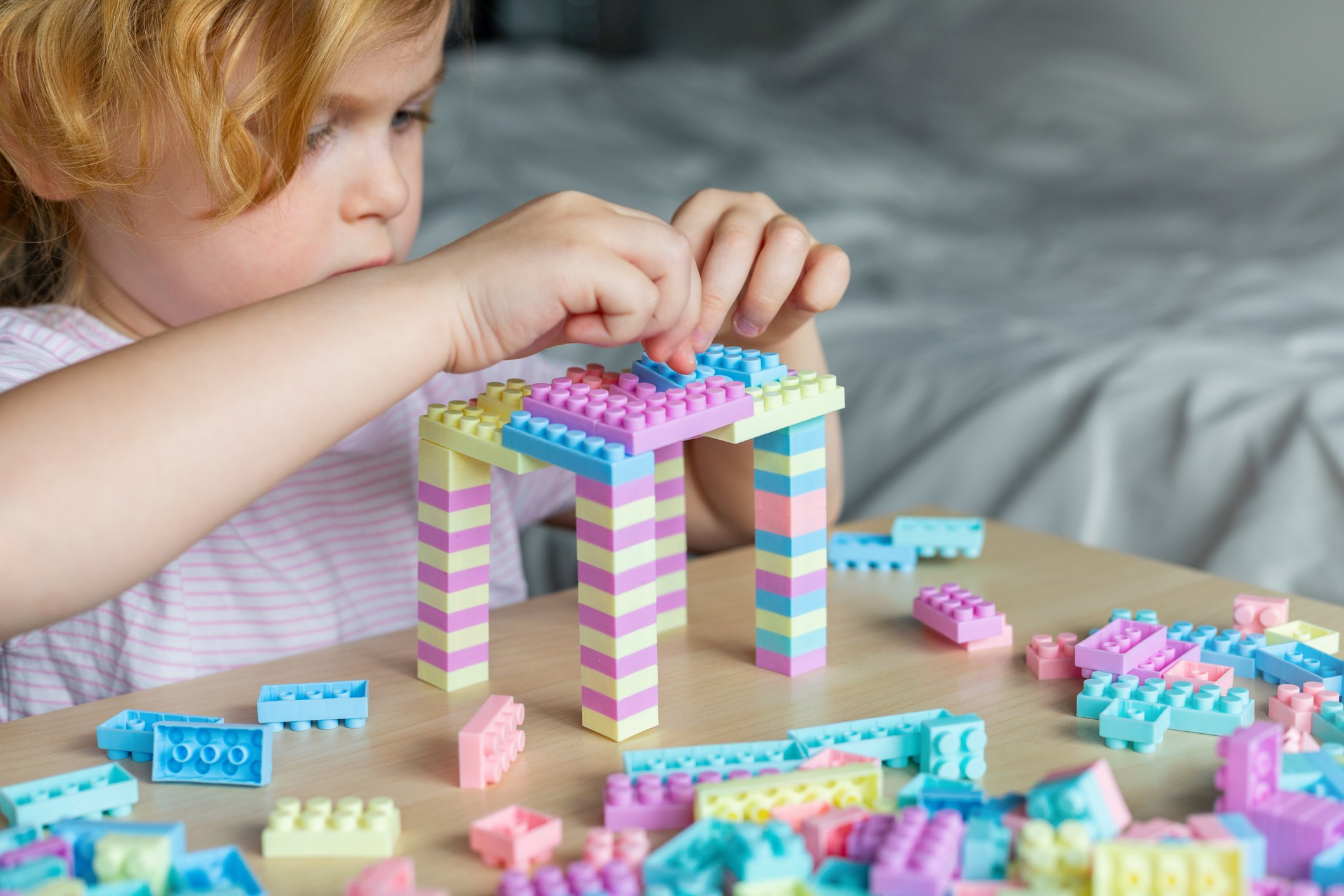 Little beautiful child playing with toy plastic building blocks, sitting at the table. Small girl busy with fun creative leisure activity. Development of fine motor skills for children.