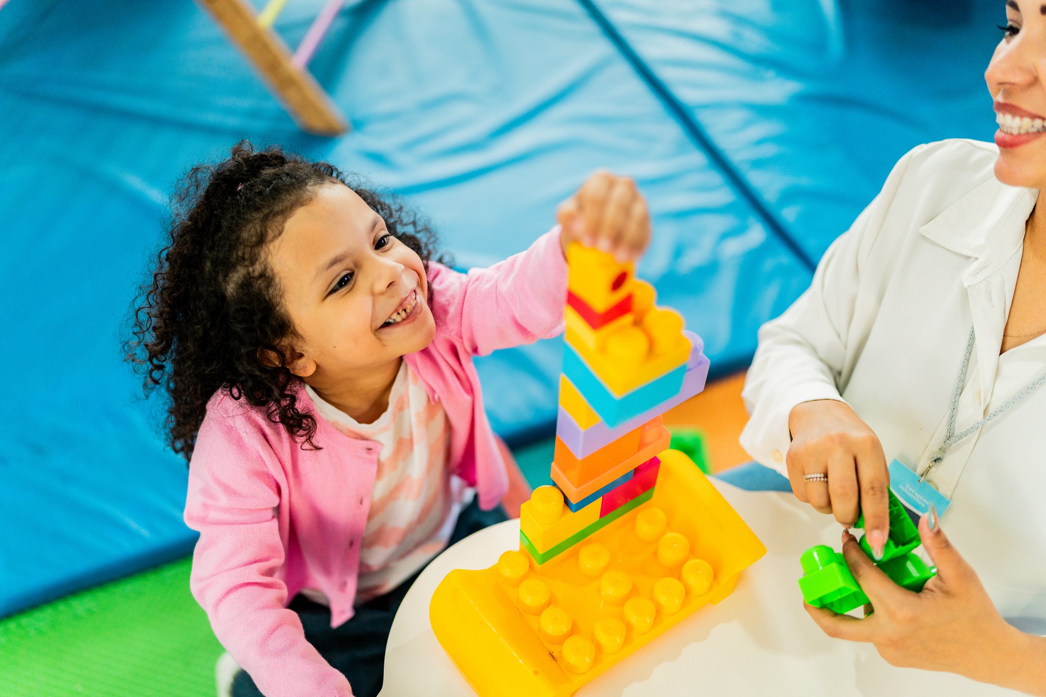Child girl and teacher playing with toy blocks at playroom
