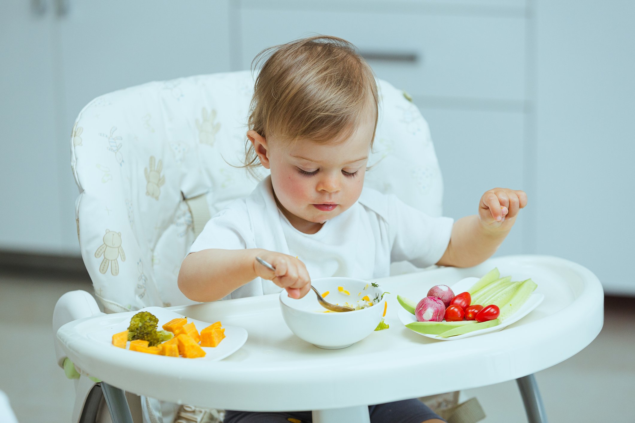 Adorable caucasian toddler girl eats vegetables on her own, pricking them with hands. The concept of self-feeding. BLW.