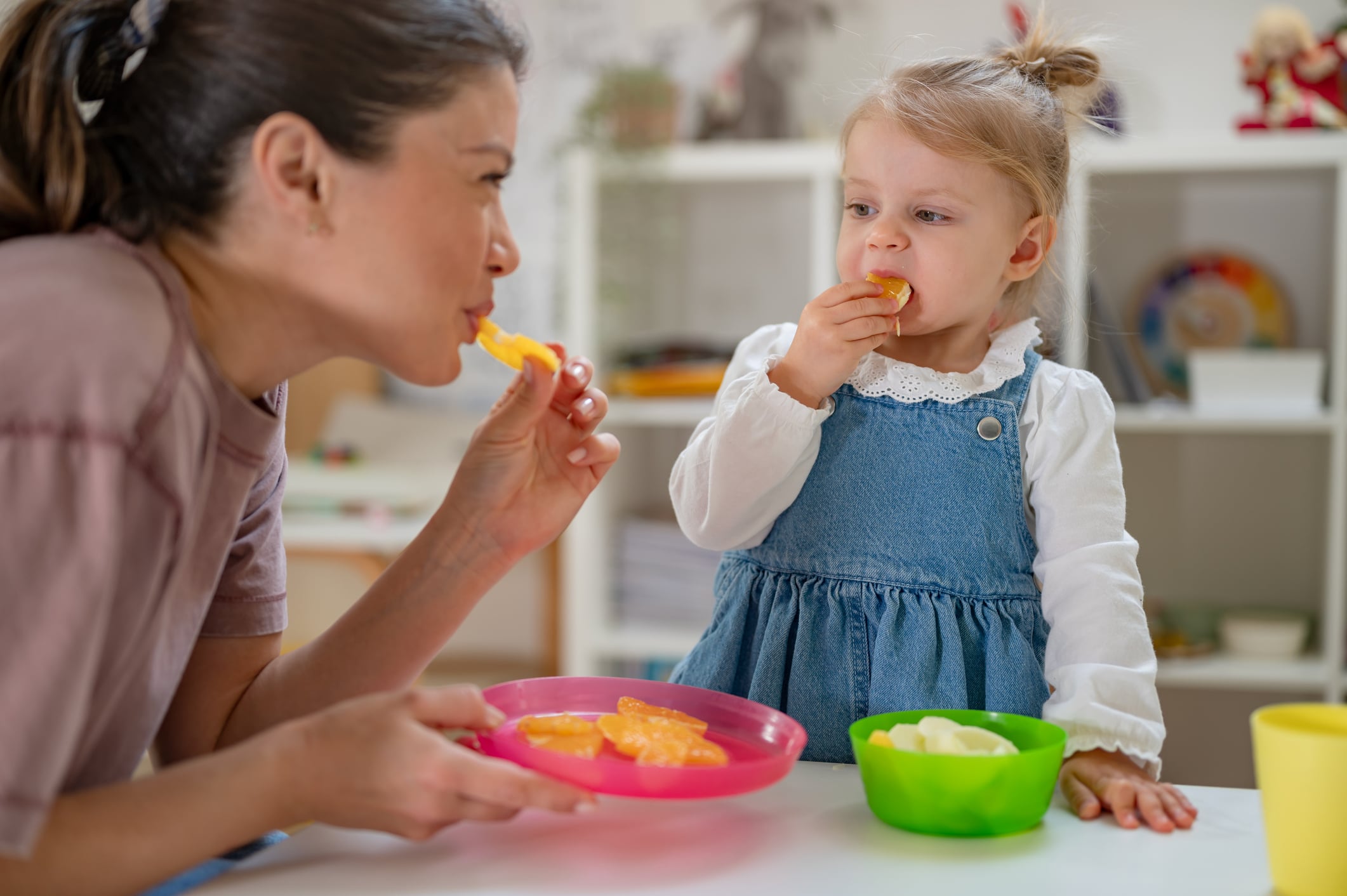 A mother and her young daughter enjoy a healthy snack together, eating fresh fruit in a bright and cozy home setting